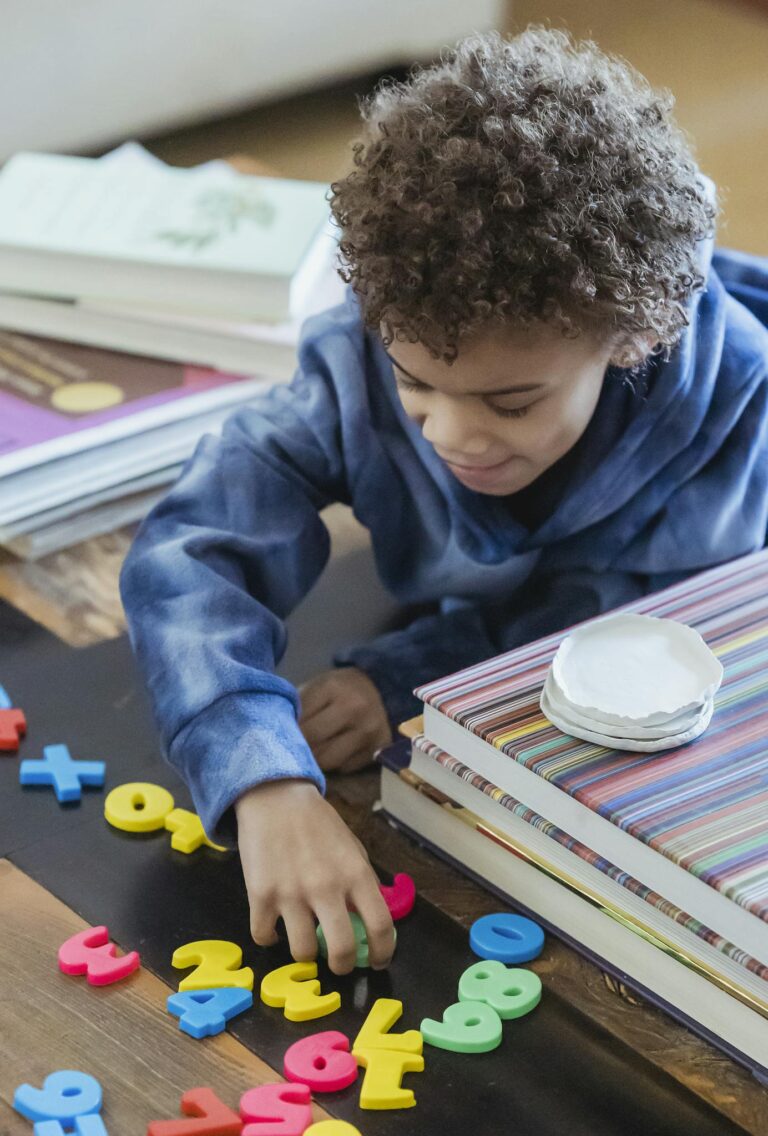 Ethnic kid with Afro hairstyle playing with colorful toy numbers and letters in house room
