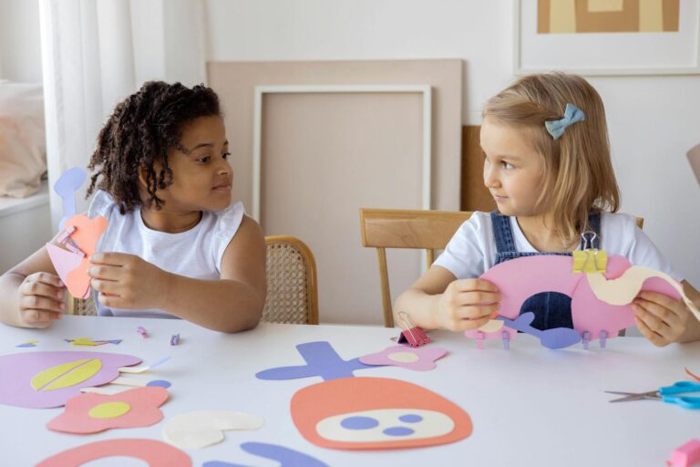 Two children having fun with arts and crafts, creating paper cutouts indoors.